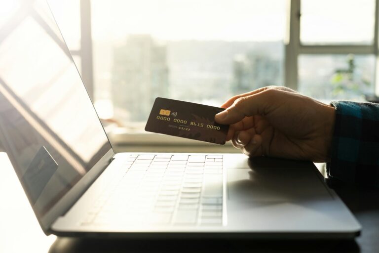A hand holding a credit card in front of a laptop, symbolizing online shopping and digital payment.