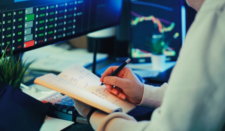 Person analyzing financial data on screens, making notes. Ideal for business and finance themes.
