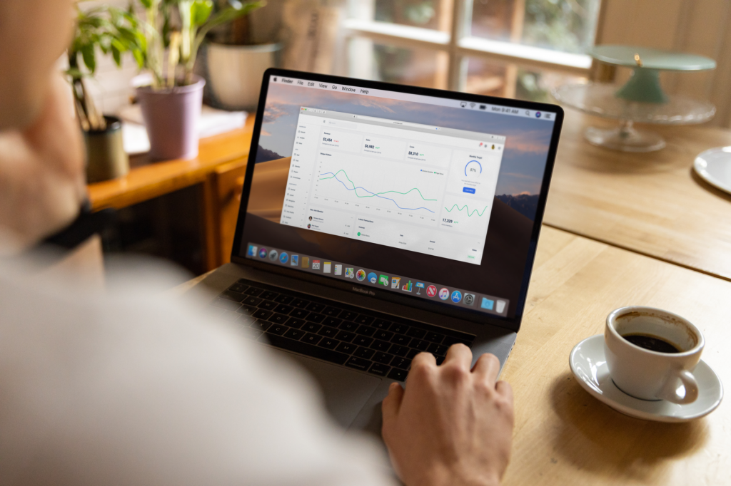 Person analyzing stock market data on laptop indoors with a casual setting and coffee.