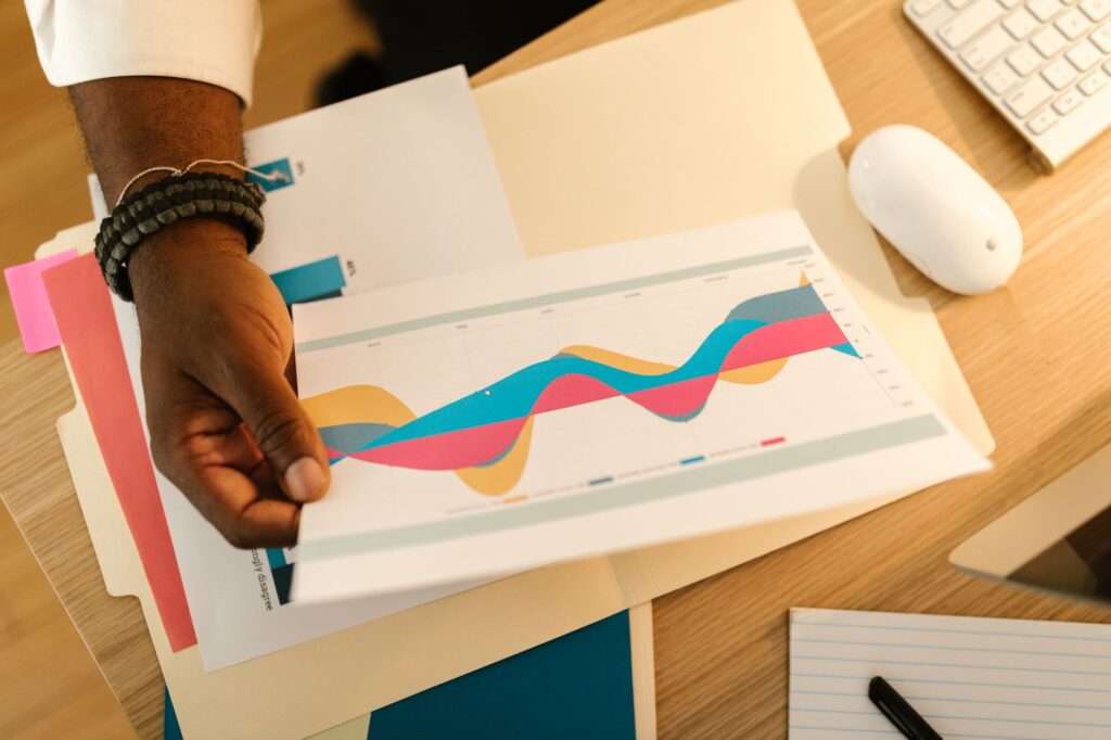 A person's hand holds a printed business graph paper on a desk with office supplies.