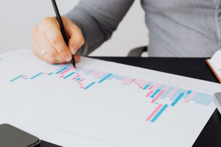 Close-up of a man writing on a printed chart indoors, analyzing colorful data.