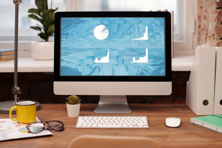 Stylish home office setup with desktop, plant, and eyeglasses on a wooden desk.